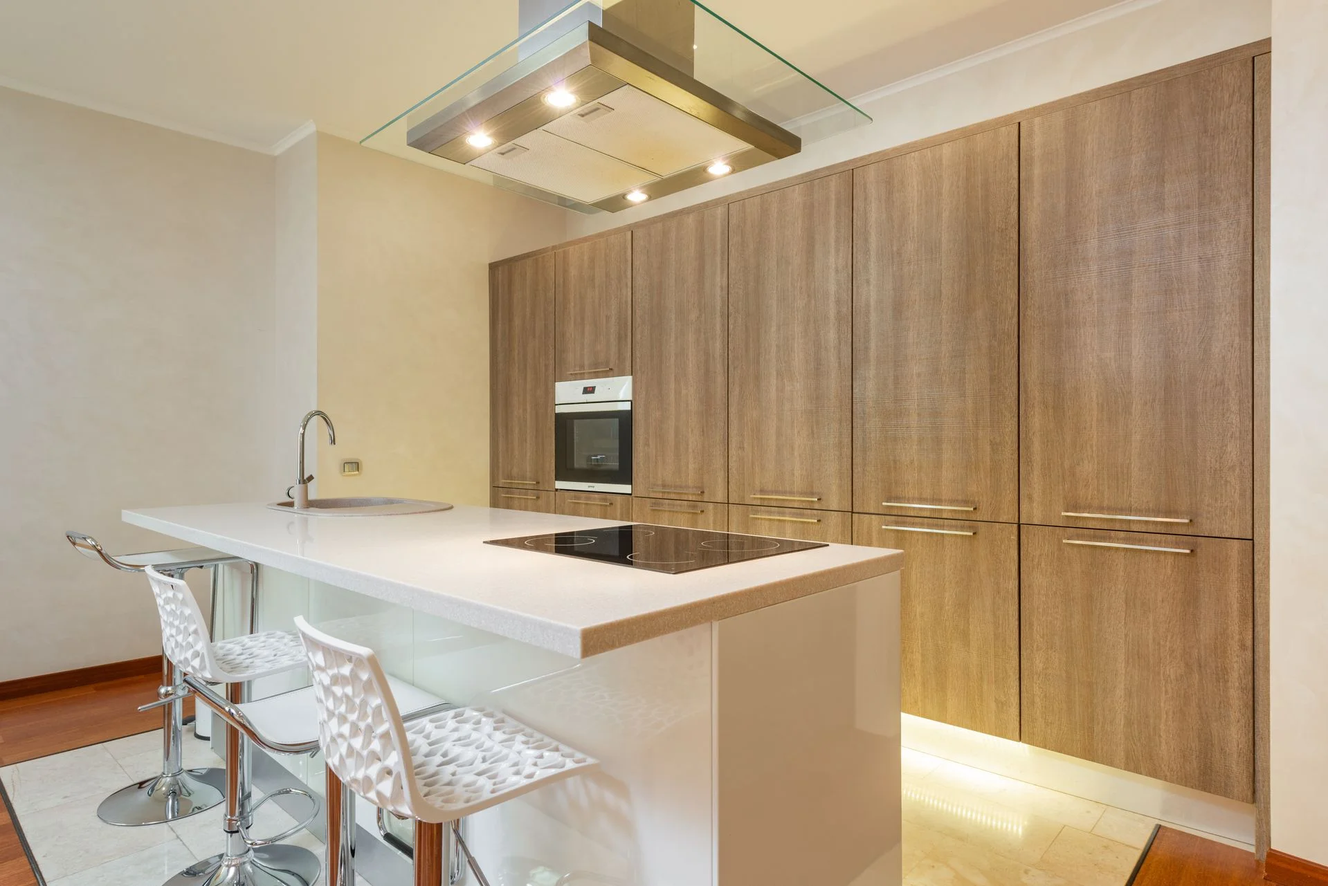 Vista de una cocina panelada con armarios de madera texturizada, una isla central blanca con placa de inducción y taburetes altos, ideal para cocinas ocultas