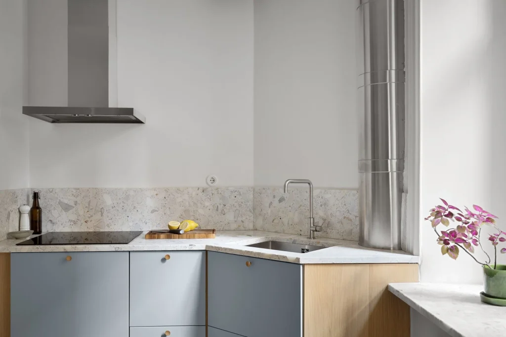 cocina con muebles azules y encimera de cuarzo gris clara con detalles de grifería y campana en acero inoxidable 