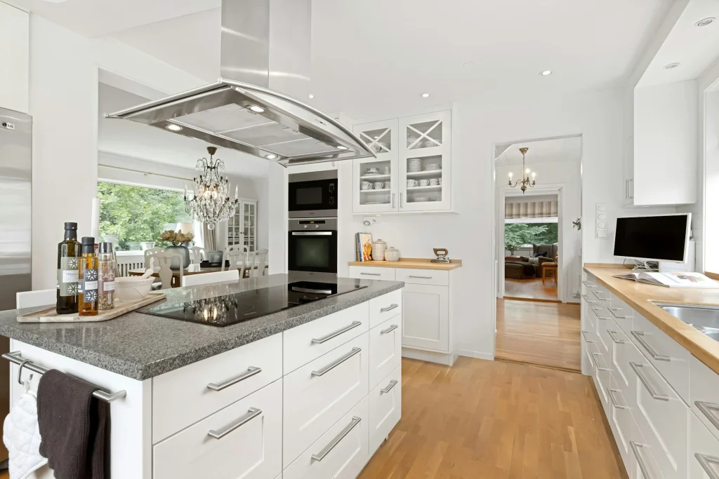 cocina con isla con encimera de granito y encimera de madera maciza para el resto de estancias con muebles blancos tradicionales y detalles en acero inoxidable