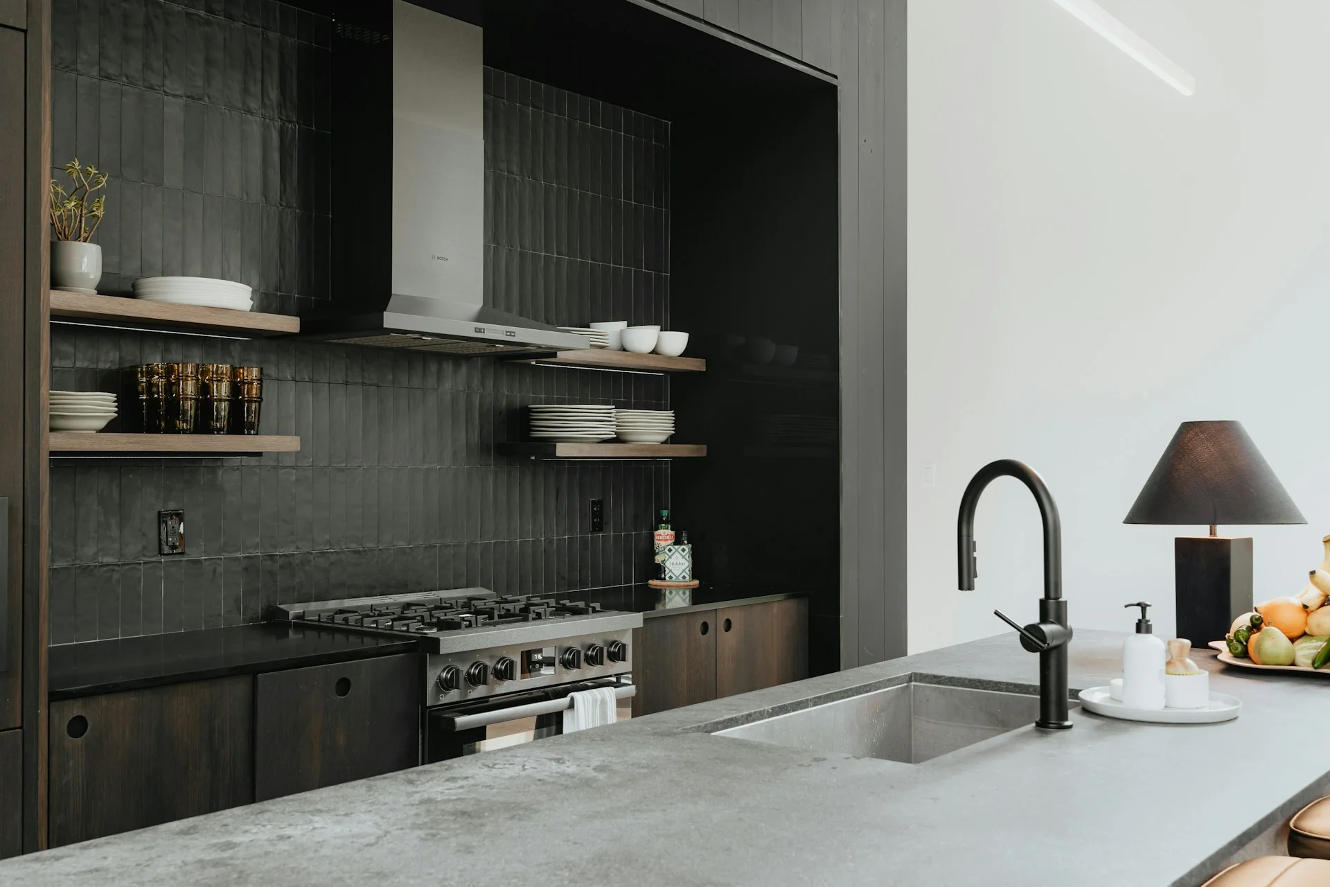 Cocina moderna con encimera de microcemento oscura en la isla con fregadero integrado y grifería negra, combinada con muebles oscuros y azulejos negros texturizados