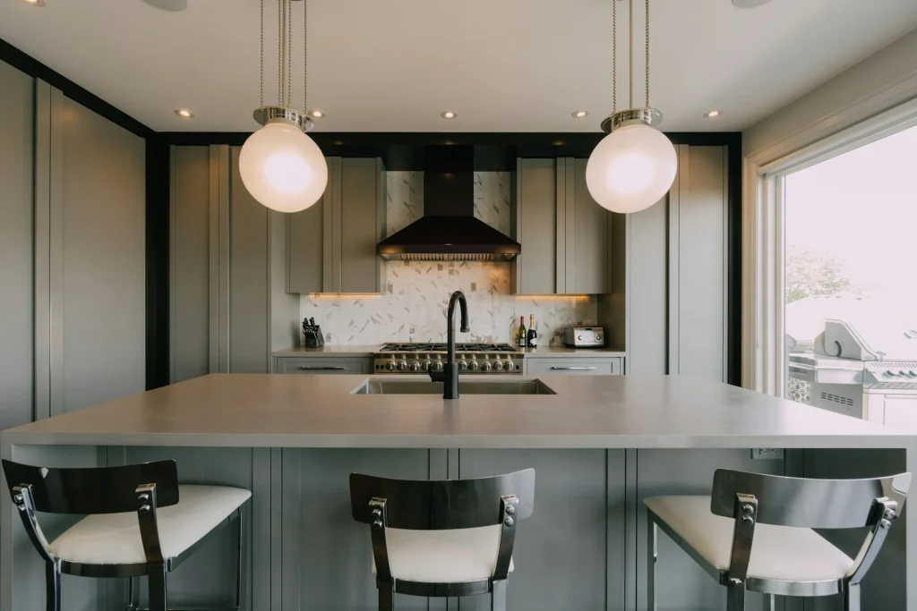 Reforma de cocina contemporánea que destaca por una isla con encimera de microcemento gris, fregadero bajo encimera y taburetes modernos a juego