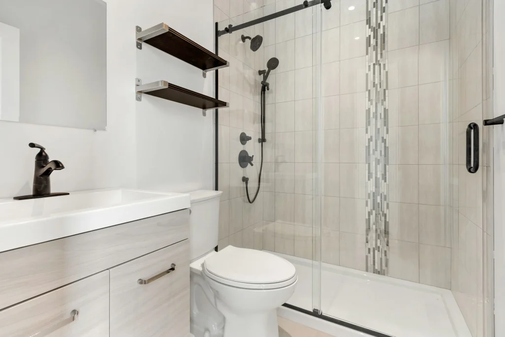Baño contemporáneo equipado con una mampara corredera de cristal con perfilería y tirador negros sobre una ducha integrada con revestimiento de azulejos claros