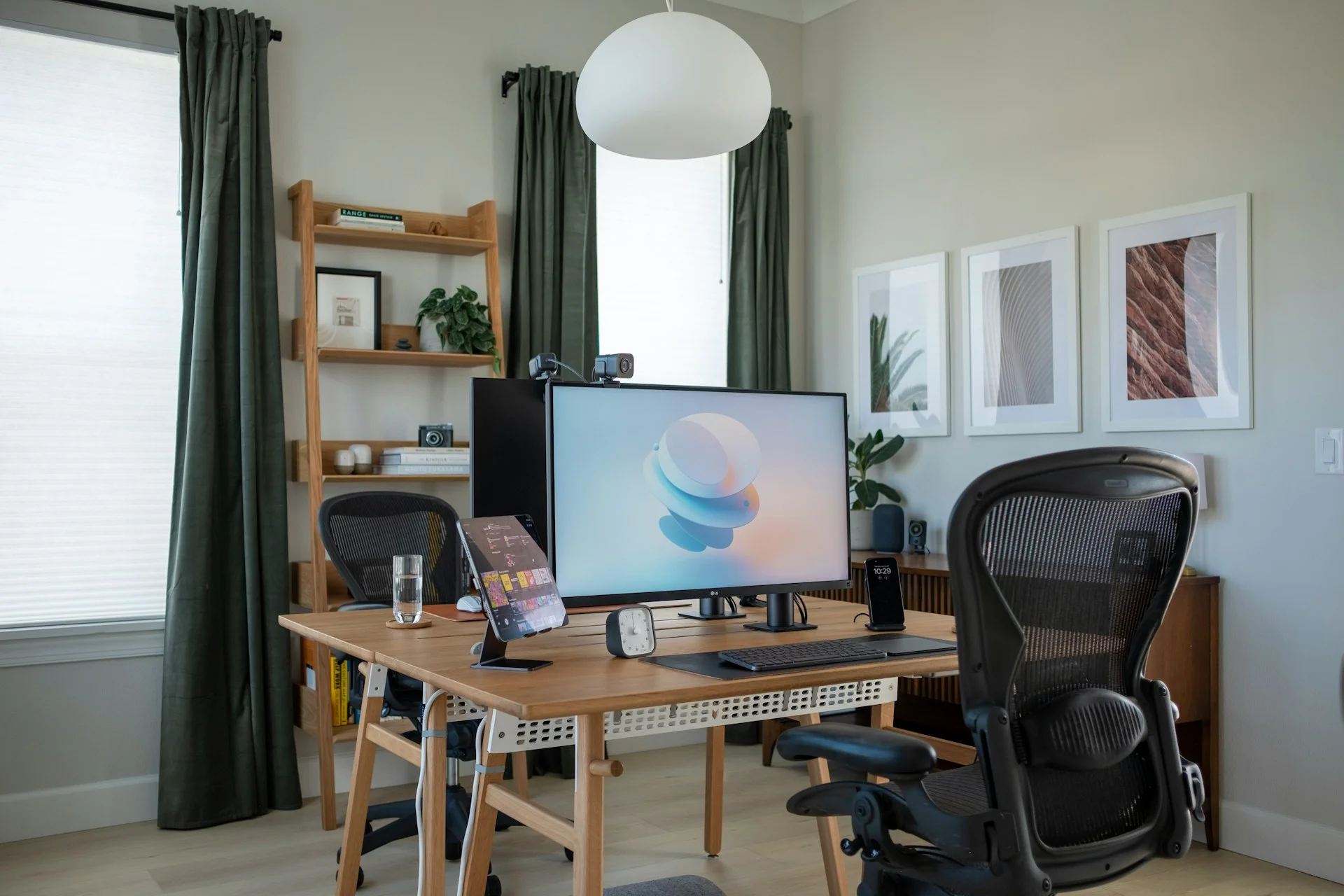 Oficina en casa luminosa con escritorio de madera central, silla ergonómica de malla, monitor principal y estanterías en un diseño moderno