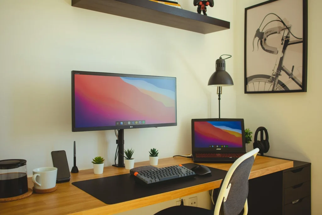 Habitación convertida en oficina en casa de estilo nórdico y minimalista, con un gran escritorio de madera en el centro, silla de oficina ergonómica, monitor con webcam, lámpara colgante blanca y cortinas oscuras.